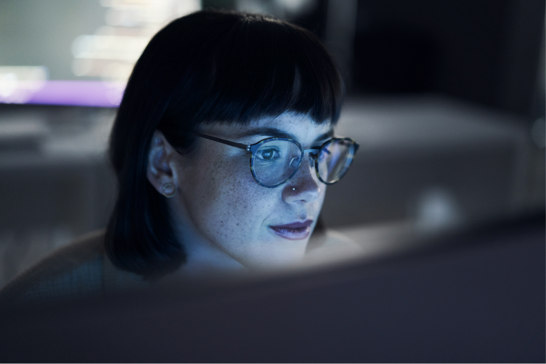 A person with glasses and wearing a shirt, is focused on a computer screen.